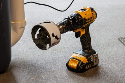 Hole saw on a Dewalt drill sitting on a garage floor.