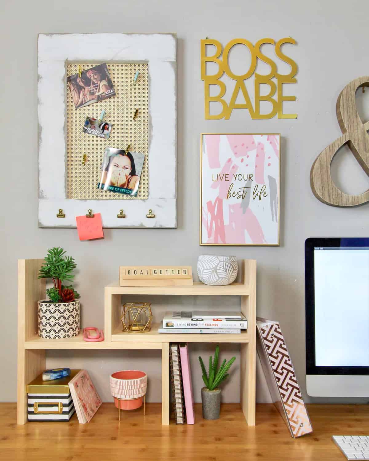 Adjustable wooden desktop organizer features succulents, notebooks, small decorative jars, black & white striped paper box, small books, letter board, keyboard and monitor in background.