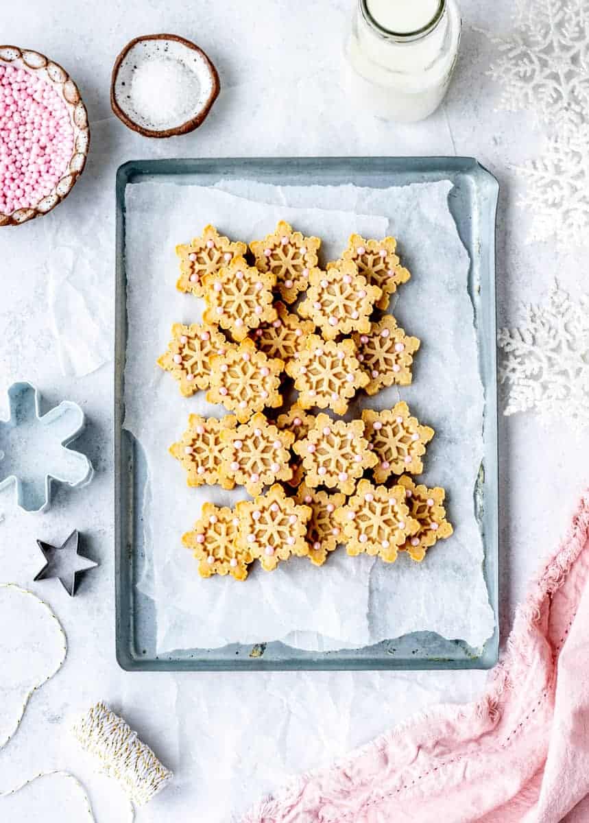 Almond flour shortbread cookies in snowflake shapes on a sheet pan.
