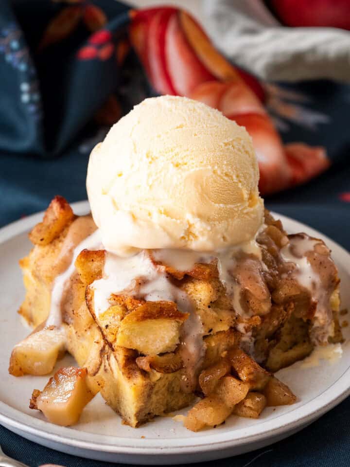 A slice of apple bread pudding with ice cream on top. Background of napkins and a small plate.