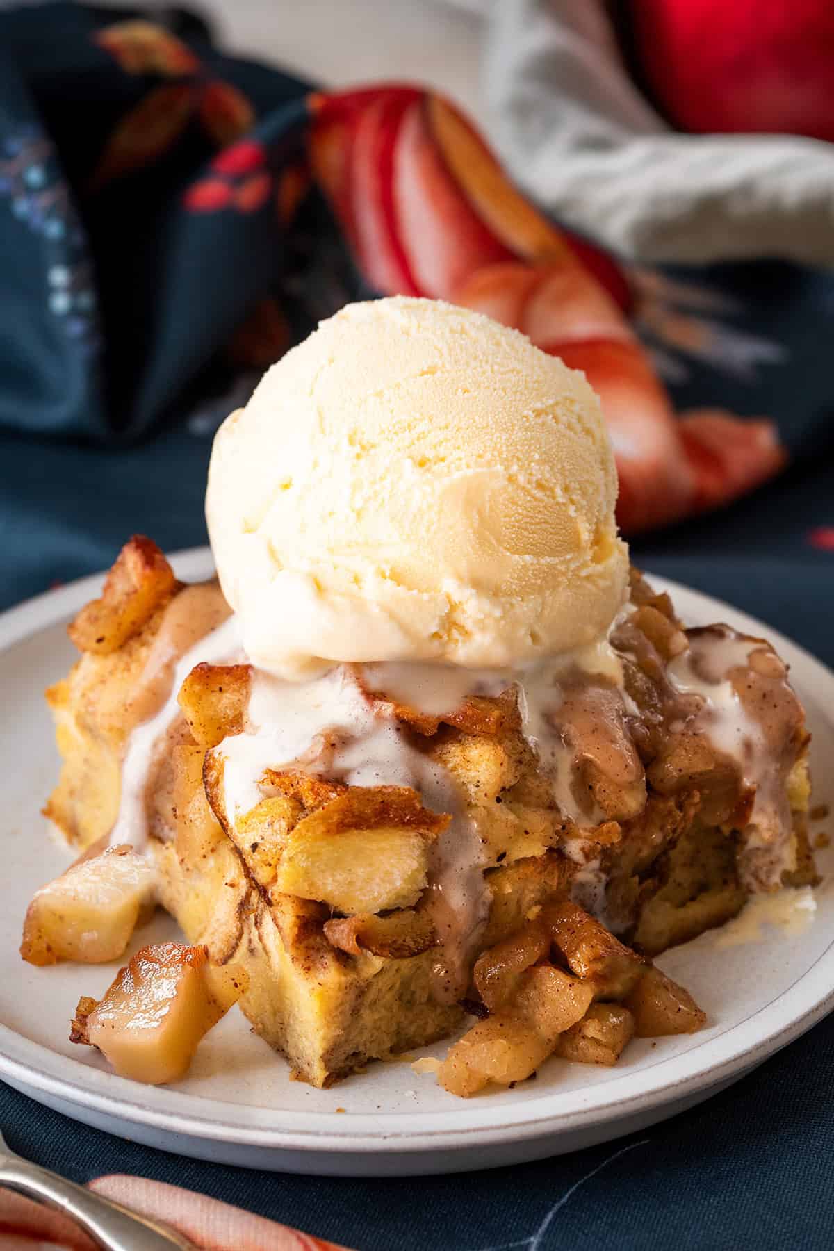 A slice of apple bread pudding with ice cream on top. Background of napkins and a small plate.