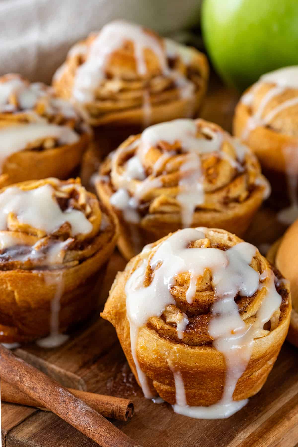 Several cinnamon rolls with cream cheese icing on a wood cutting board.