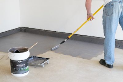 Man painting a garage floor with a roller.