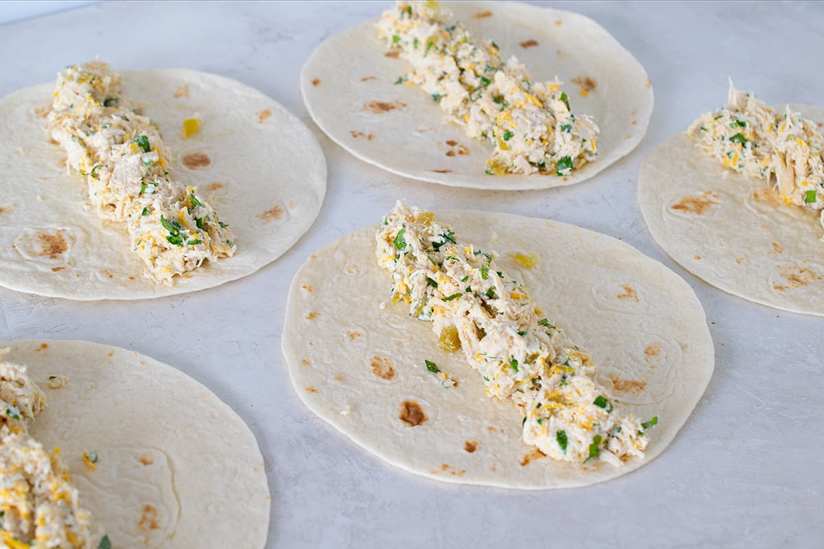 Chicken enchilada filling on flour tortillas before rolling.