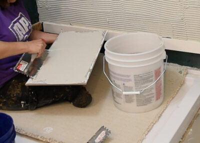 Woman back buttering large tile to hang on a shower wall.