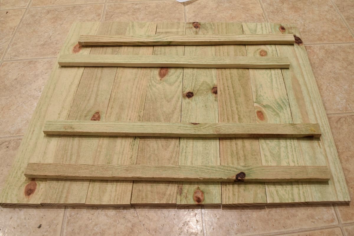 Back of natural wood plank sign on beige tiled floor.