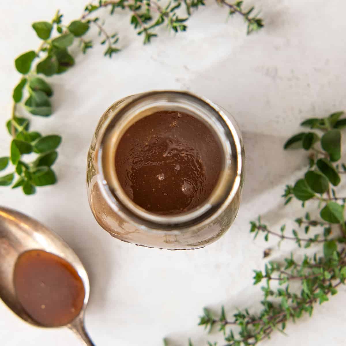 Looking into a jar of homemade Balsamic Vinaigrette with a spoon and herbs around.