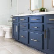 Midnight blue vanity with brass handles in a grey and white bathroom.