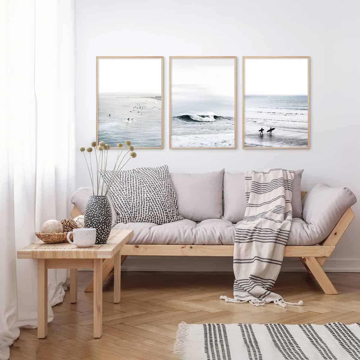Living room view of couch with three seascape photos and surfers in them.