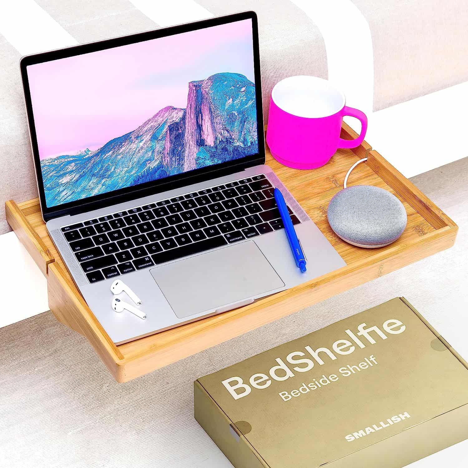 Removable wooden bed shelf holding laptop, pen, earbuds, and pink coffee mug.