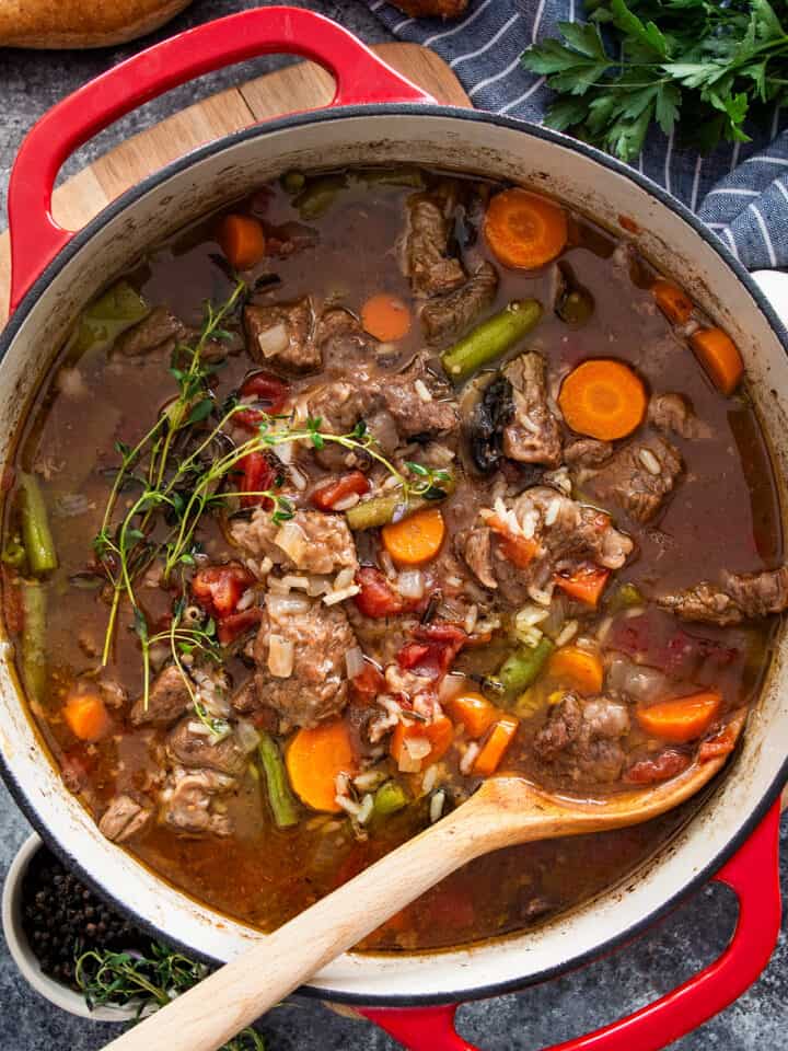 A large pot of beef and rice soup with vegetables and a wooden spoon.