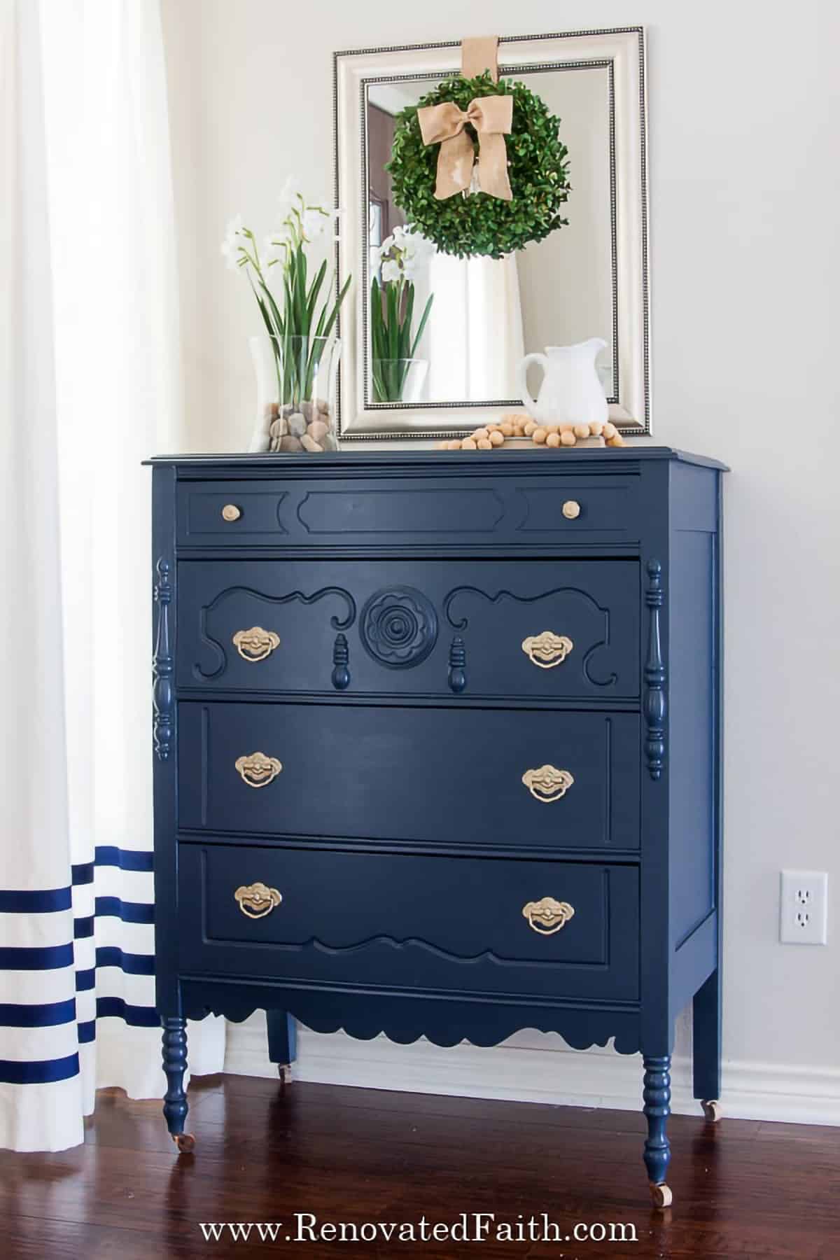 Painted Navy dresser with silver hardware decorated with a mirror.