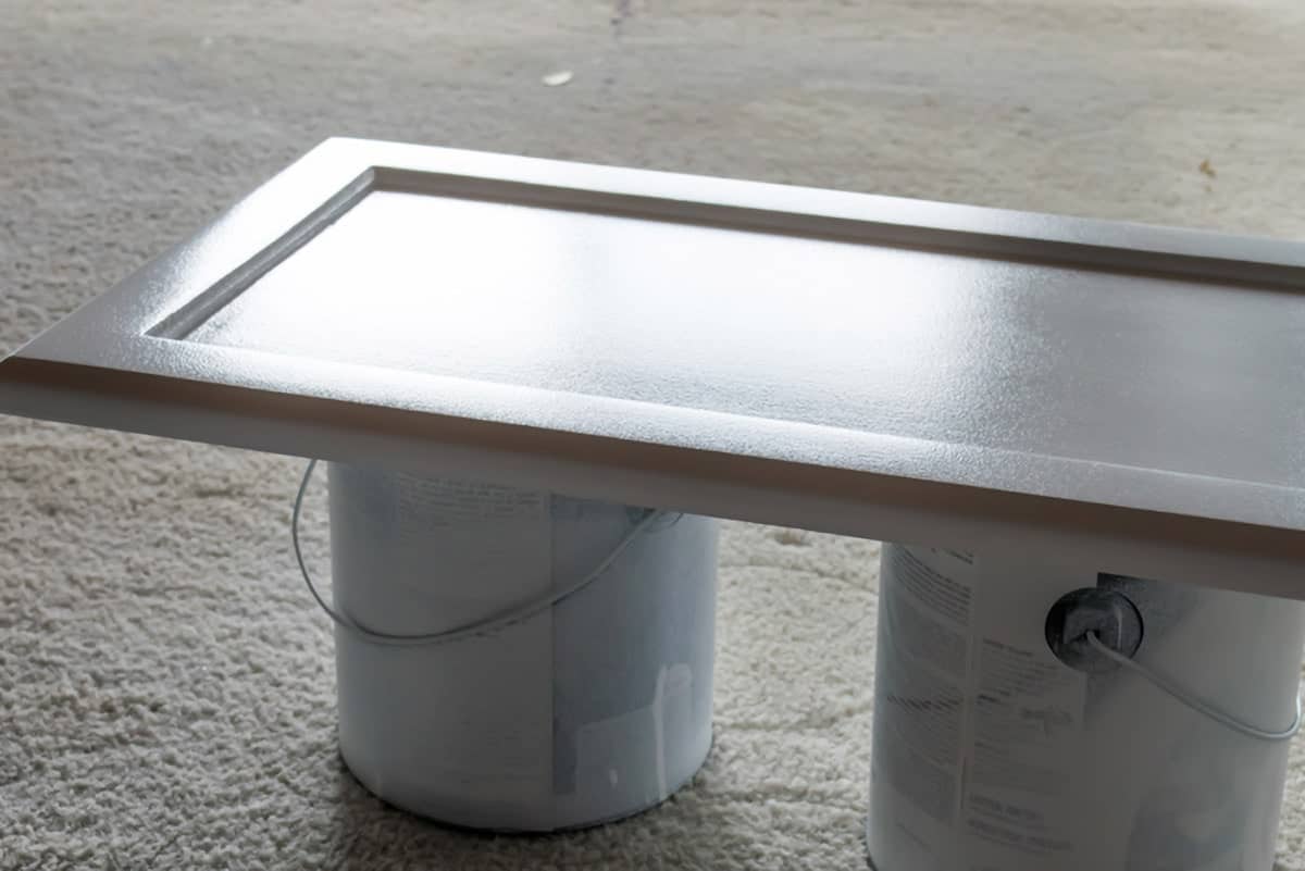 Two paint cans on carpet supporting white door cabinet with protective clear coat.