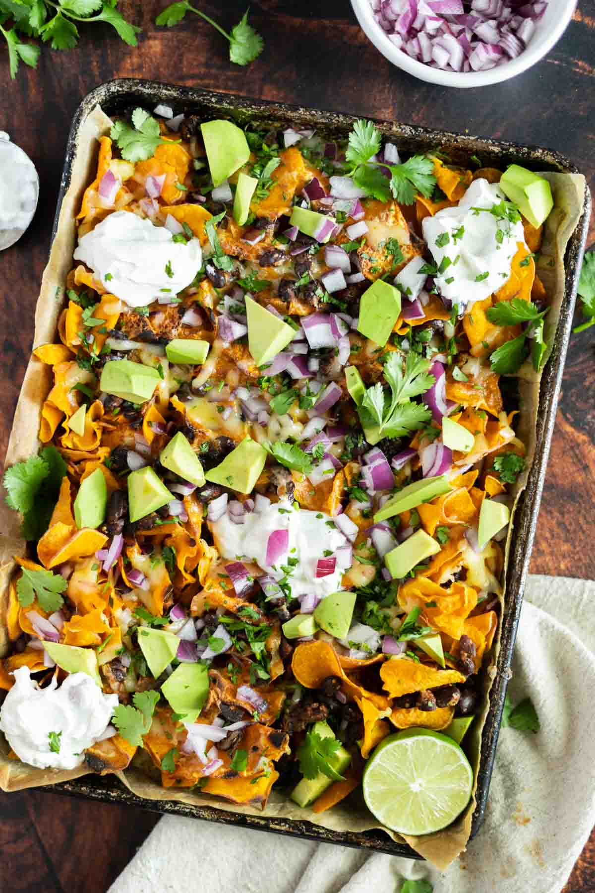 Baking pan with sweet potatoes topped with nacho toppings like beans, beef, avocado, and sour cream.