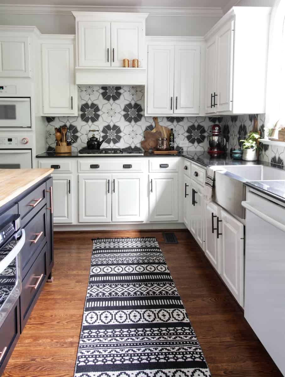 Spacious kitchen with white cabinets, navy blue island, black and white backsplash tile, and detailed rug.