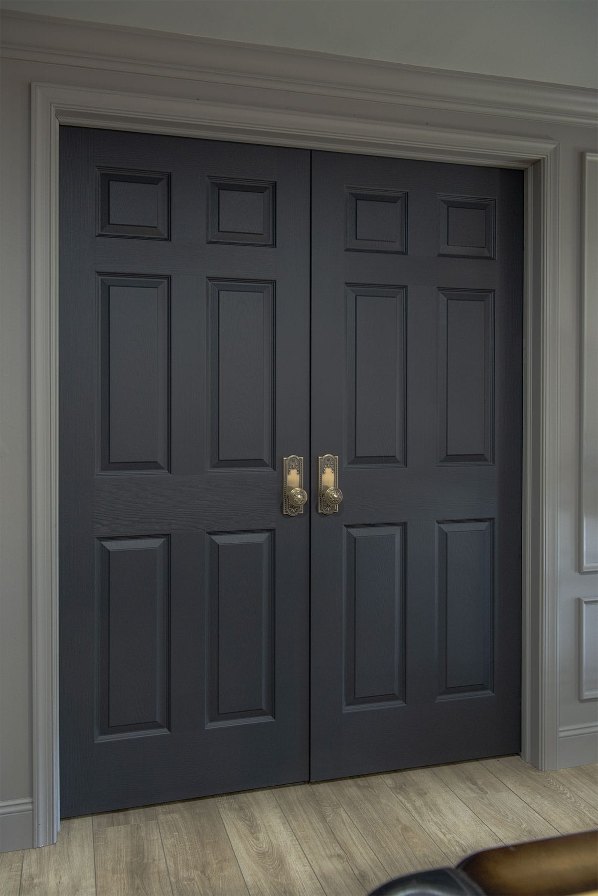 Interior double doors painted charcoal black with brass doorknobs in a moody gray room.