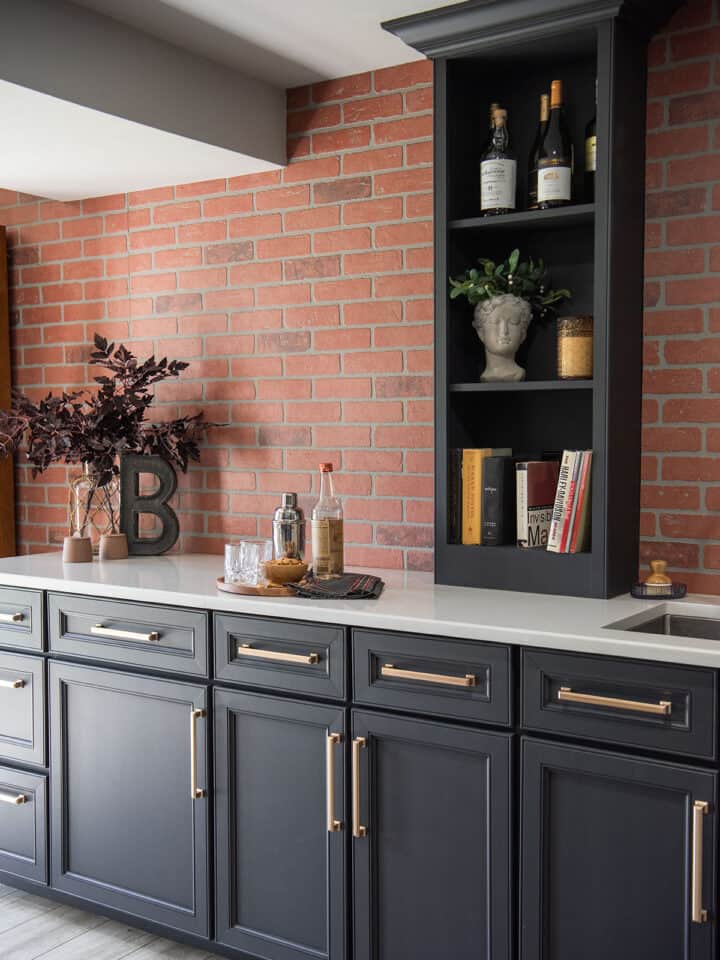 Wet bar with black cabinets, brick wall in a contemporary style for a pub inspired industrial basement makeover.