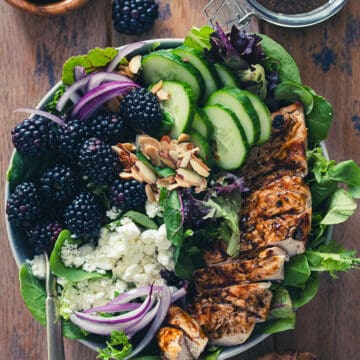 Top down flat lay of blackberry chicken salad with balsamic dressing and basil in the background.
