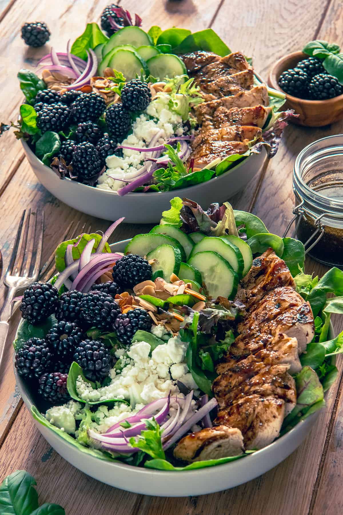 Two bowls of Chicken salad with almonds, blackberries, cucumbers, and goat cheese on top.