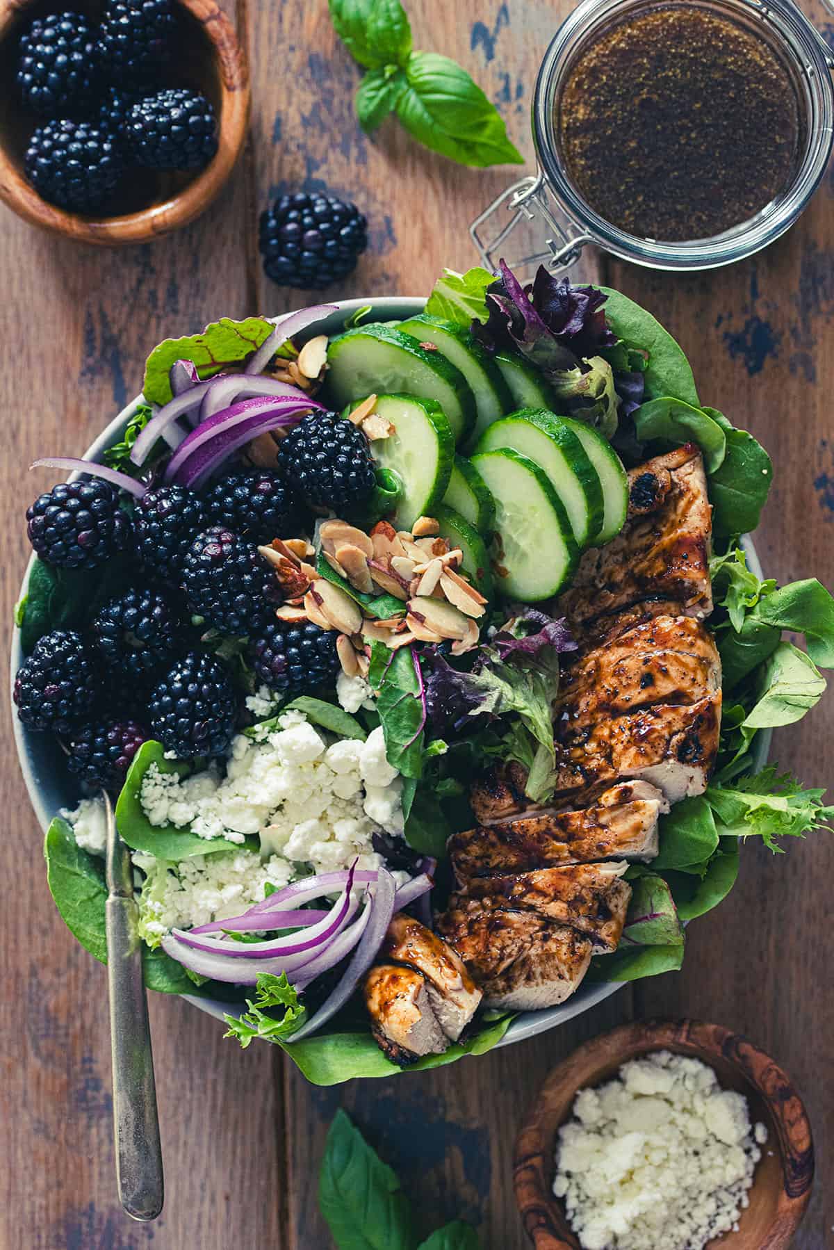 Top down flat lay of blackberry chicken salad with balsamic dressing and basil in the background.