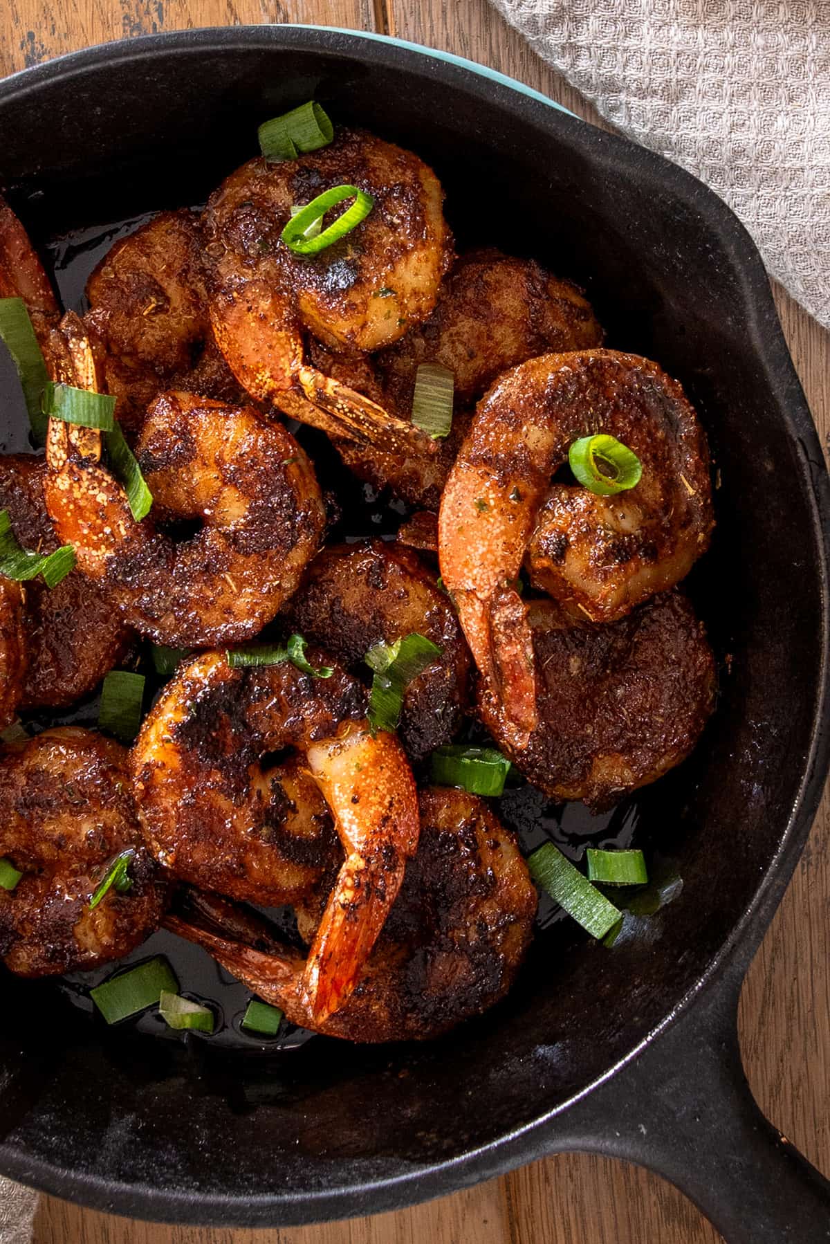 A black cast iron pan full of spicy blackened shrimp with green onions on top.