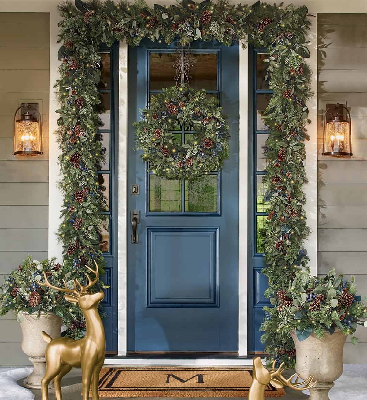 Blue front door with Christmas decorations including wreath, lighted garland, and gold deer decor.