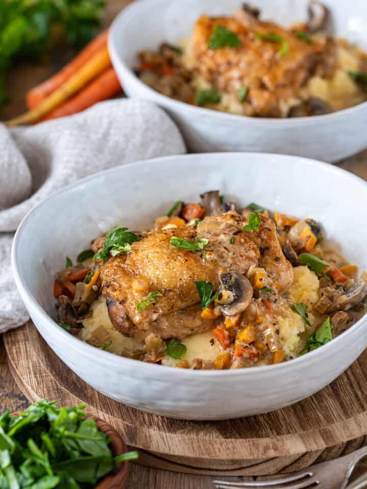 Wine braised chicken fricassee in a bowl over mashed potatoes with gravy and vegetables spooned over.