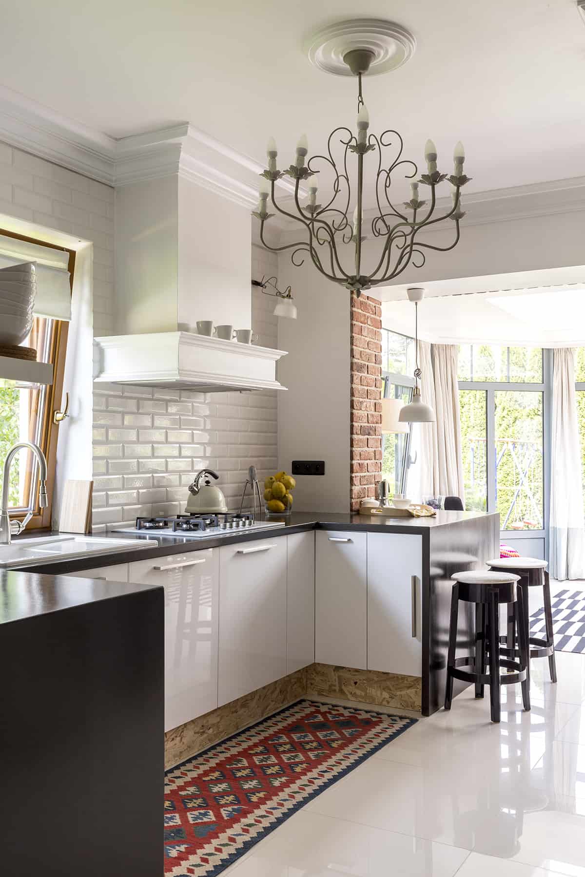 White modern kitchen with old world charm like a brick accent wall, candelabra chandelier and wood kick plate.