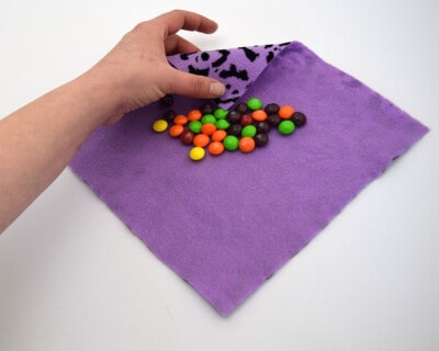 View of hand folding a purple felt square full of round colored candies.