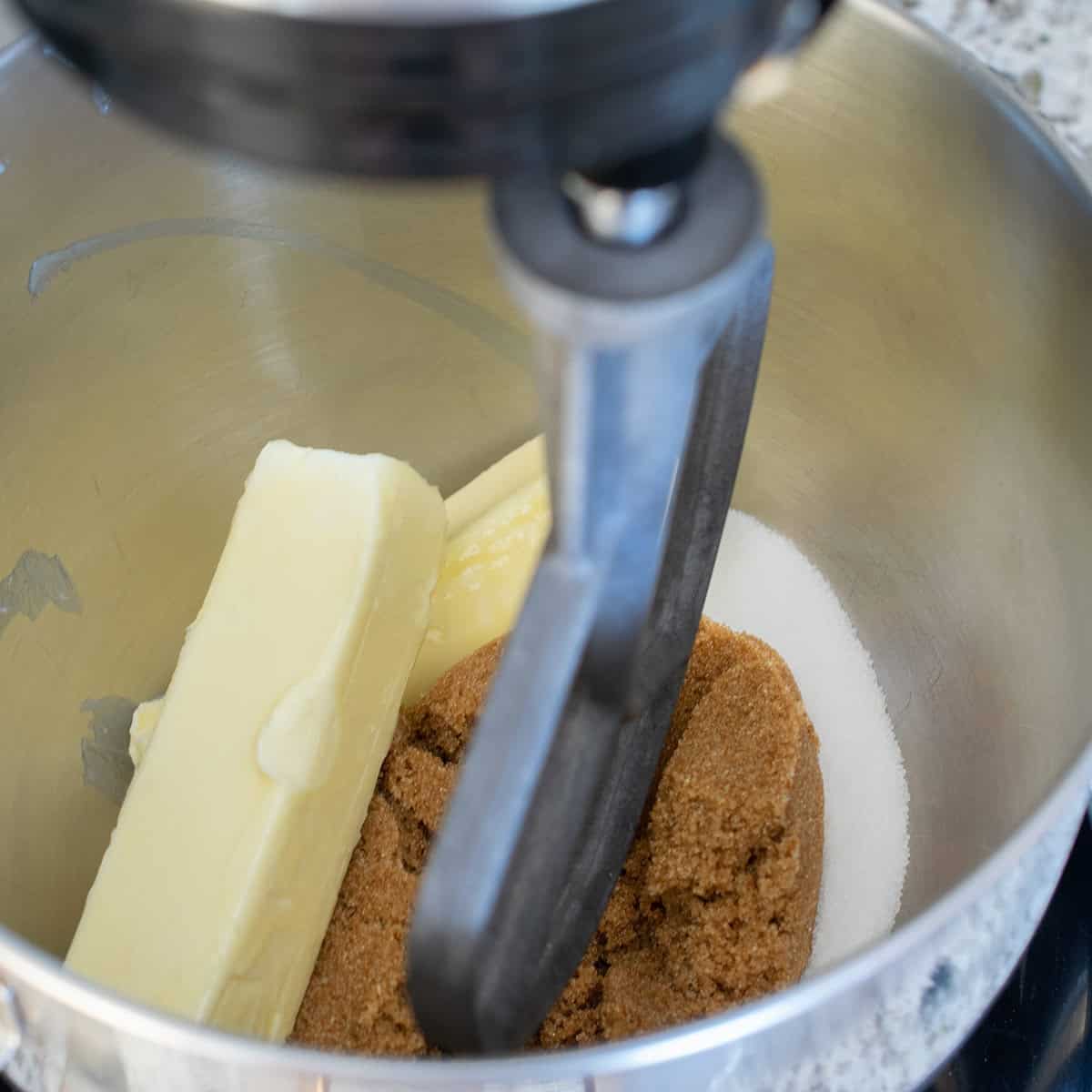 A stick of butter, brown sugar, and white sugar in a stand mixer kitchenaid.