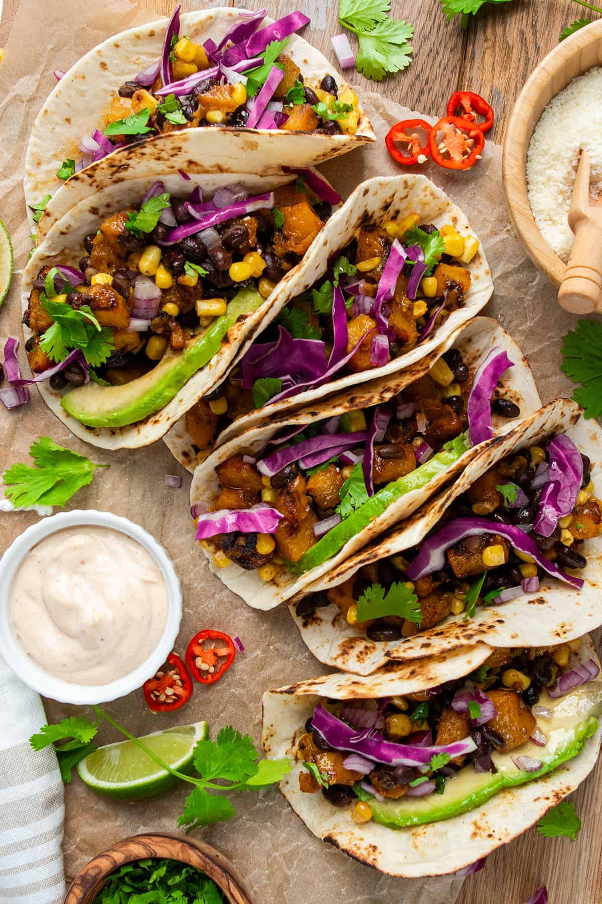 Overhead of several filled vegetarian tacos with cheese and sauces on the side.