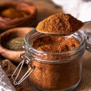 A spoonful of Cajun seasoning over top of a full spice jar.