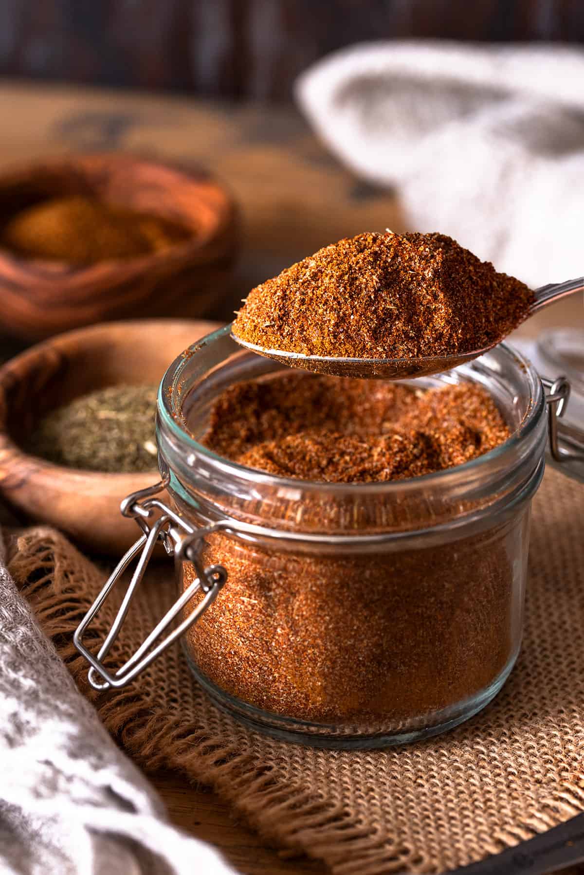 A spoonful of Cajun seasoning over top of a full spice jar.