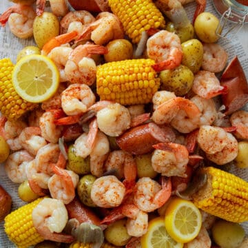 Cajun Shrimp Boil with lemons, andouille sausage, potatoes, and corn laid out on newspaper on a table.