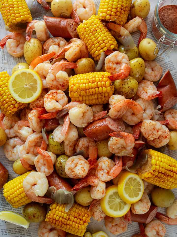 Cajun Shrimp Boil with lemons, andouille sausage, potatoes, and corn laid out on newspaper on a table.