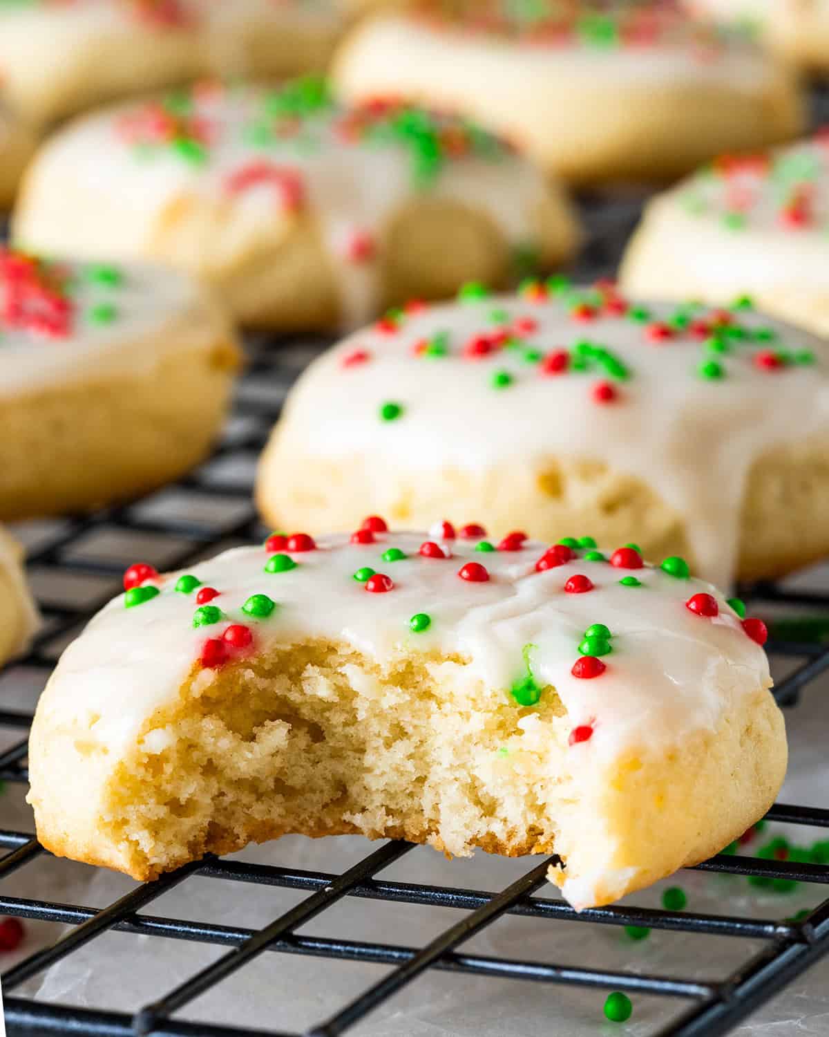 Close up of a sour cream cookie with red and green sprinkles and a bite taken out.