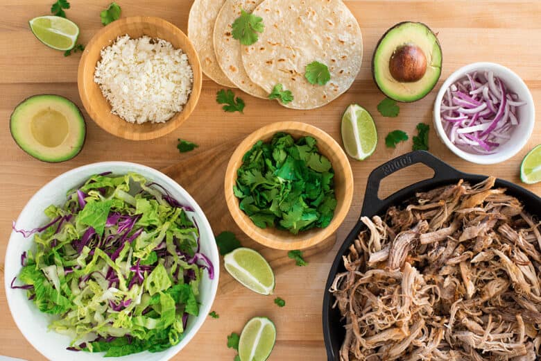 Flat lay of taco topping ideas like red onions, lime wedges, cheese, and cilantro.