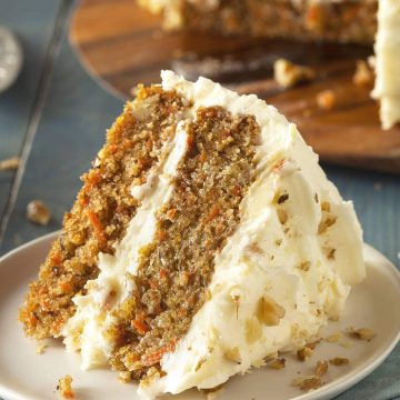 Slice of homemade carrot cake on a plate with walnuts sprinkled on top