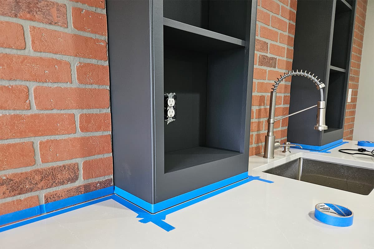 Charcoal dark cabinets and countertops with masking tape on them to add caulk around the countertops.