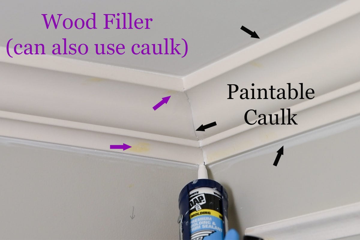 A caulk gun being used on crown molding to show where to caulk or use wood filler.
