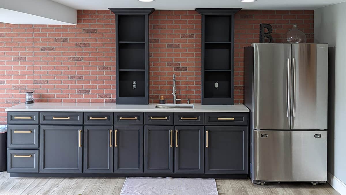 Black painted wet bar with brass handles and a brick accent wall.