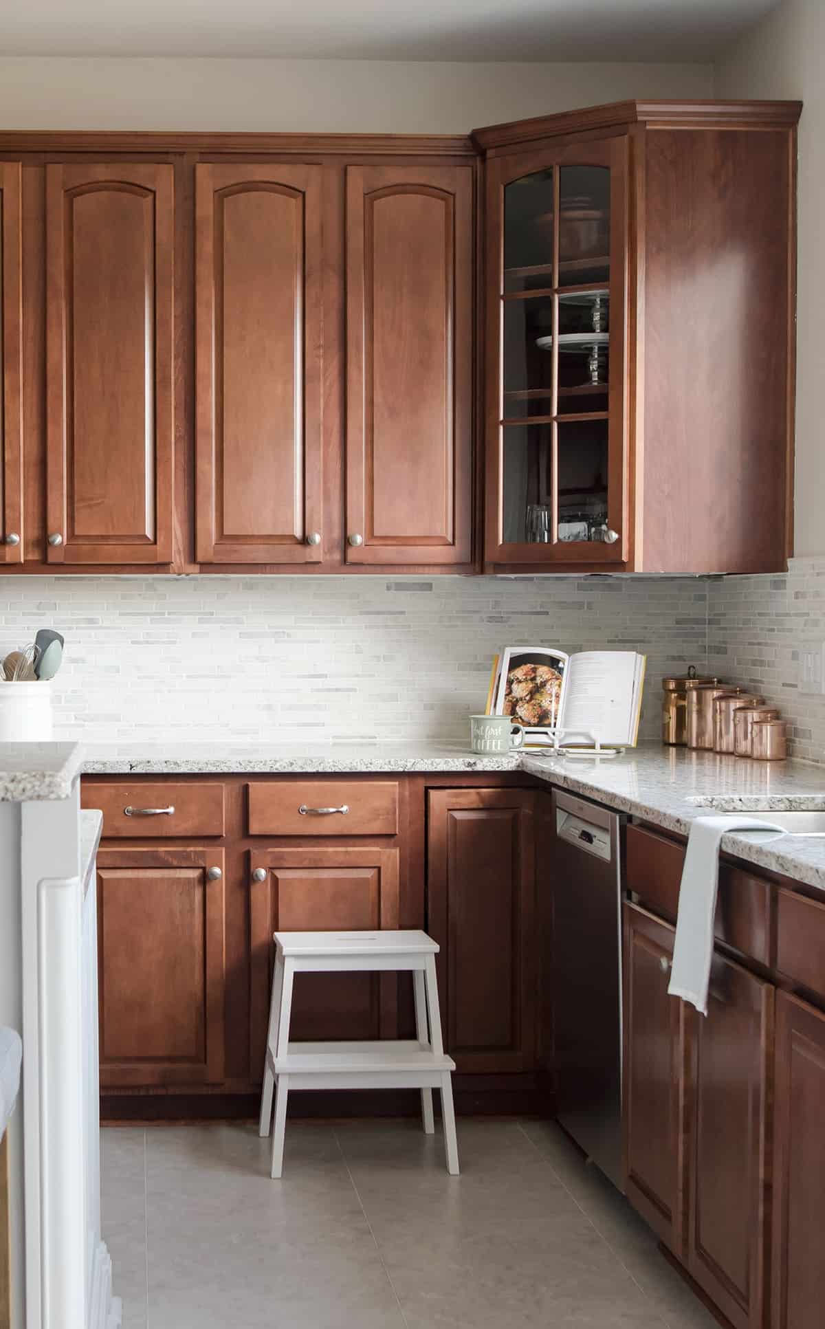 Dark wood cabinets in traditional kitchen with white and gray tile backsplash and light marble countertops.