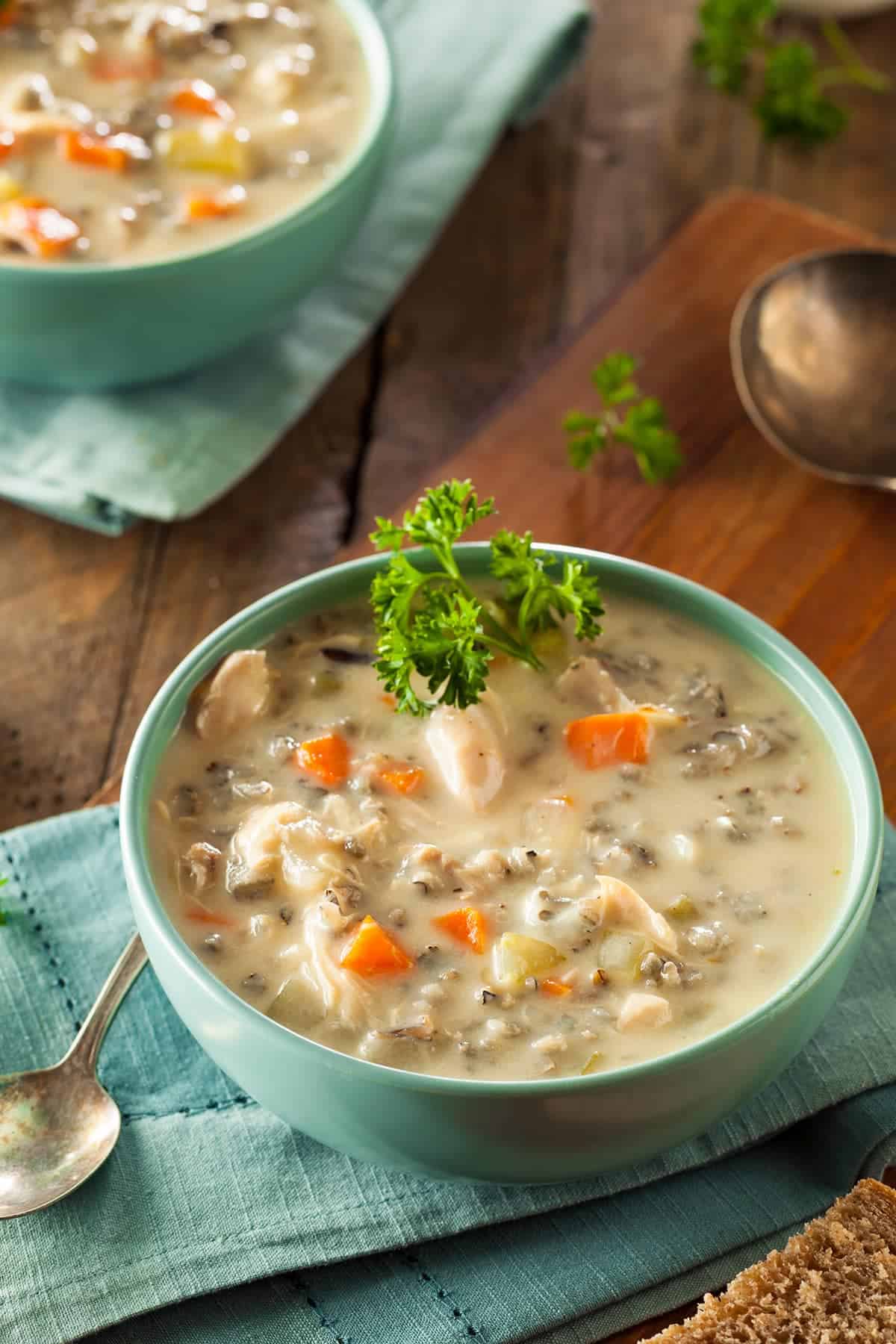 Chicken and Wild Rice soup in soup crock bowls, topped with bacon on wood surface.