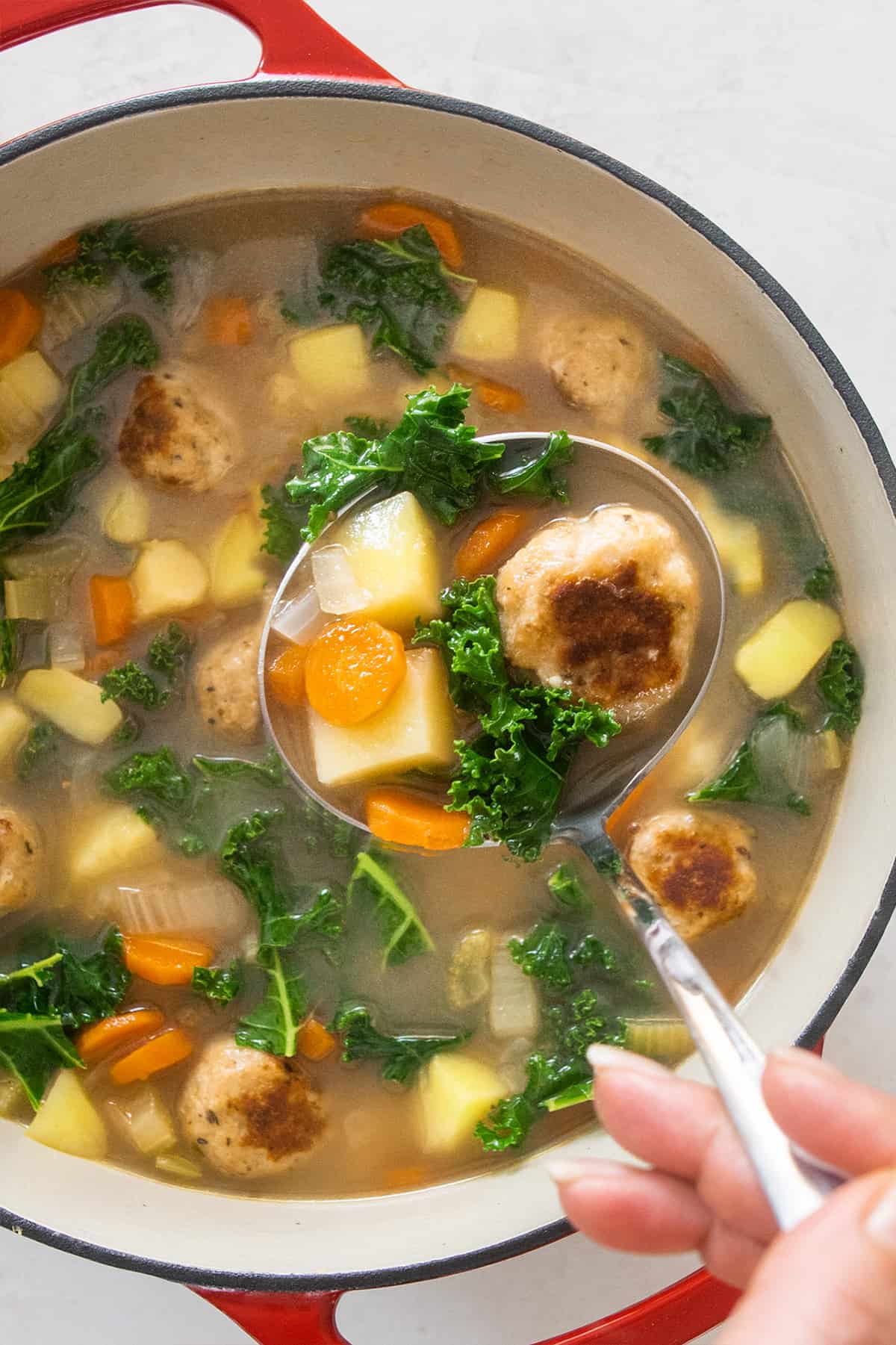 Overhead of a chicken vegetable soup pot with a ladle coming up filled with meatballs and vegetables.