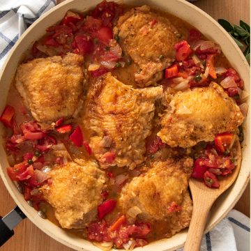 Top down shot of Chicken Cacciatore stewing in pan with tomatoes, spices, and diced onion while wood spoon stirs.