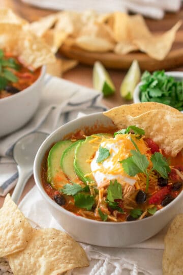 Chicken Tortilla Soup in a bowl topped with sour cream, avocado, cilantro, and cheddar cheese.