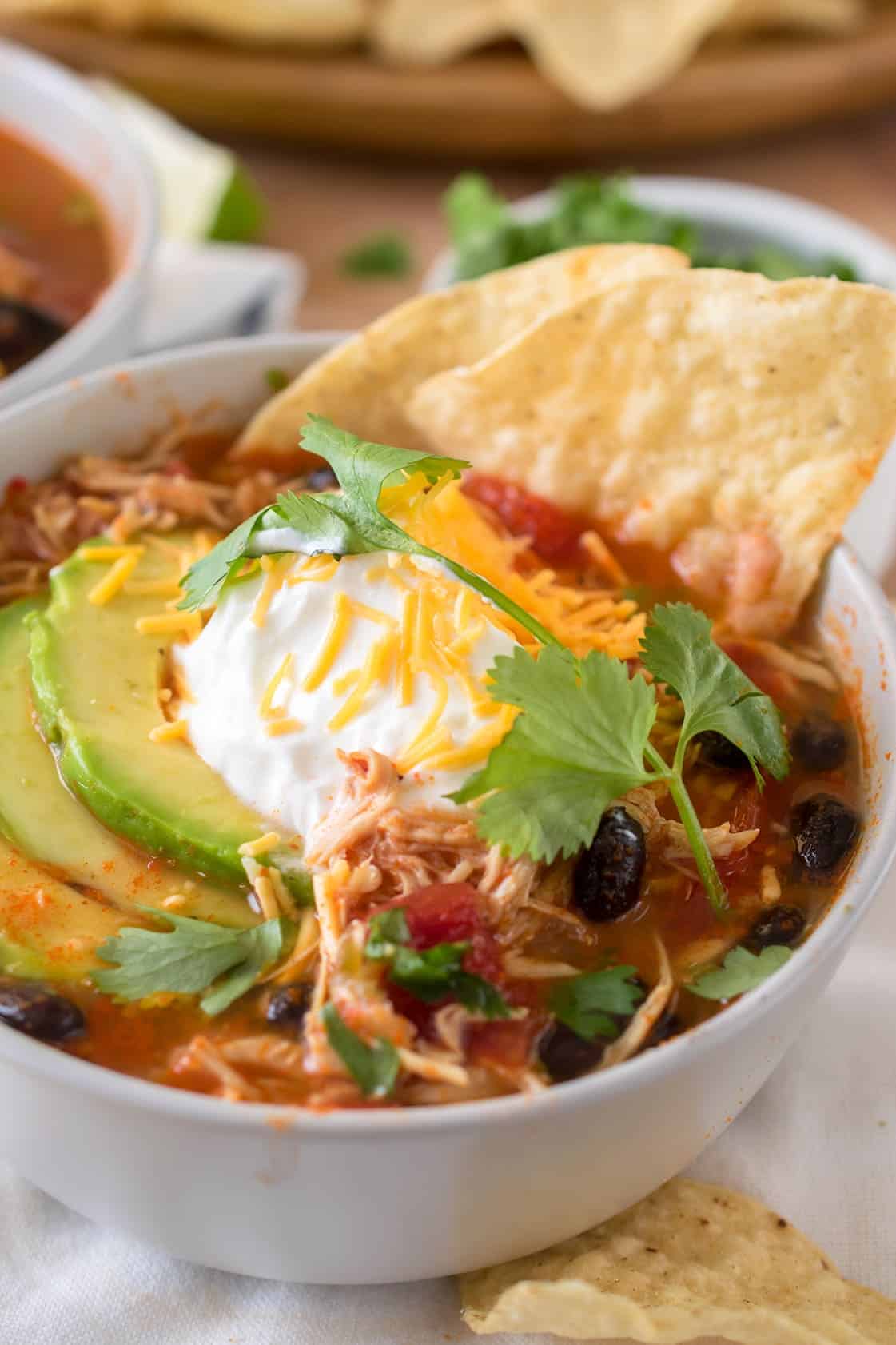 Close up of crock pot tortilla soup with black beans, tomato, cilantro, shredded cheese, avocado and tortilla chip.