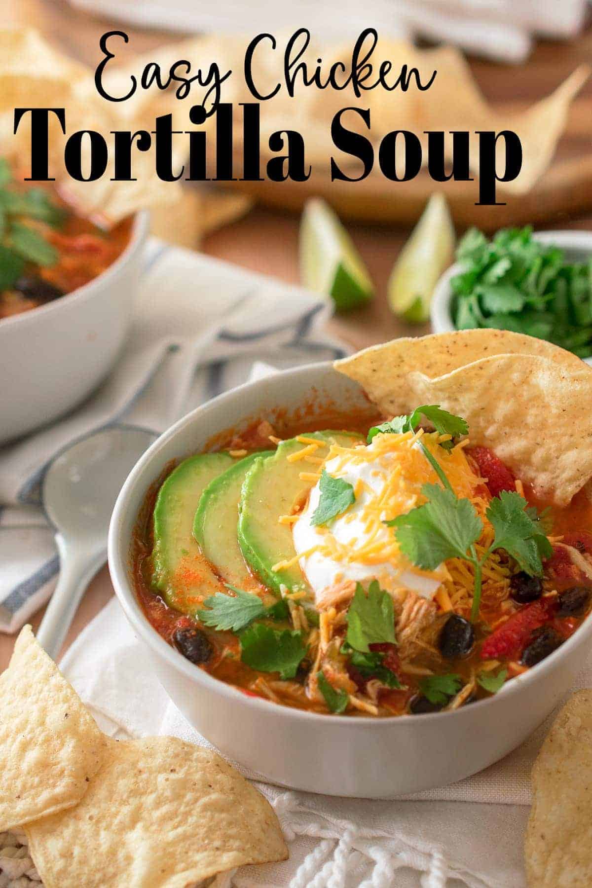 Easy Chicken Tortilla Soup topped with avocado, cilantro, cheese and sour cream with tortilla chips. Ingredients strewn around in the background and forefront.