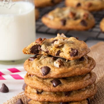 Batch of crispy chocolate chip pecan cookies freshly baked from the oven and stacked with a glass of milk.