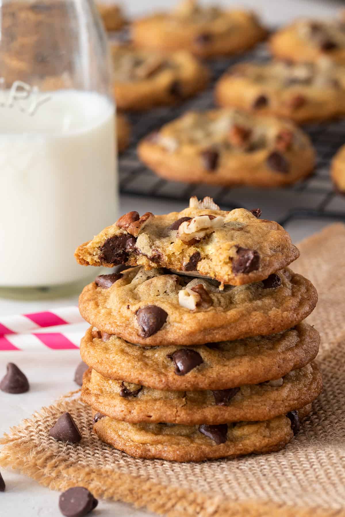 Batch of crispy chocolate chip pecan cookies freshly baked from the oven and stacked with a glass of milk.